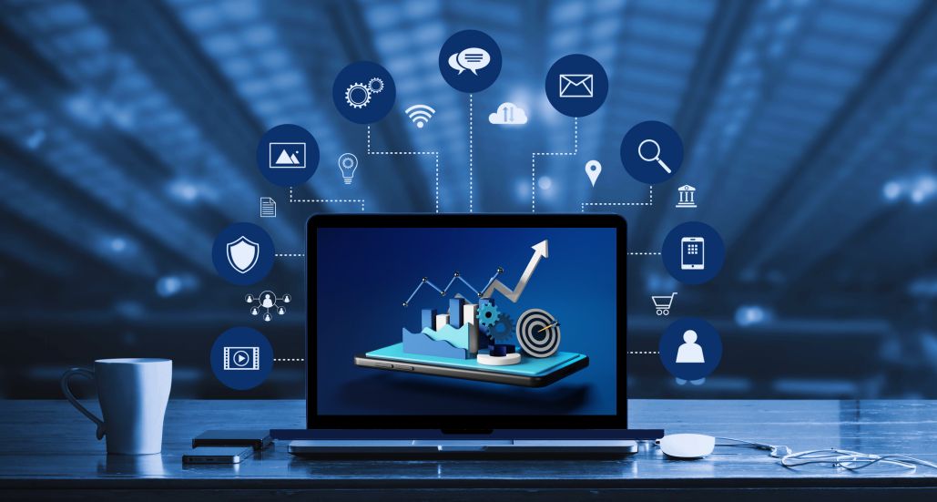 Illustration of digital marketing services, with a mug on left side and a laptop in the middle with a mouse on the right, above laptop are different emoticons of social media.